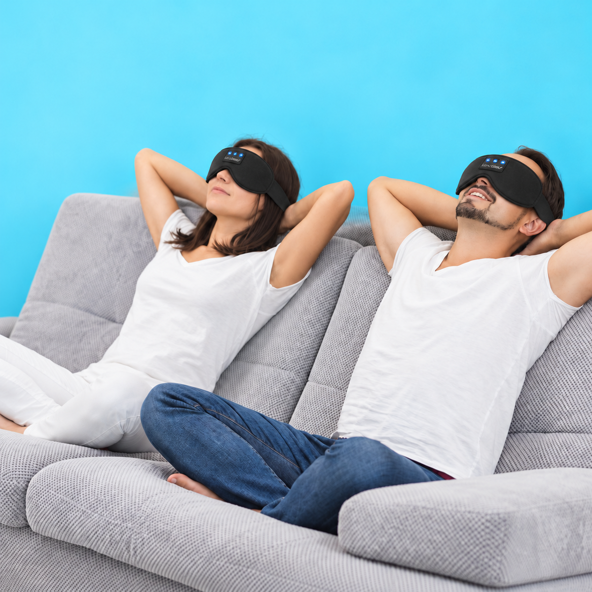 Two people relaxing on a sofa wearing black LC-dolida sleep masks