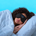Woman lying on her side in bed wearing a black Bluetooth sleep mask
