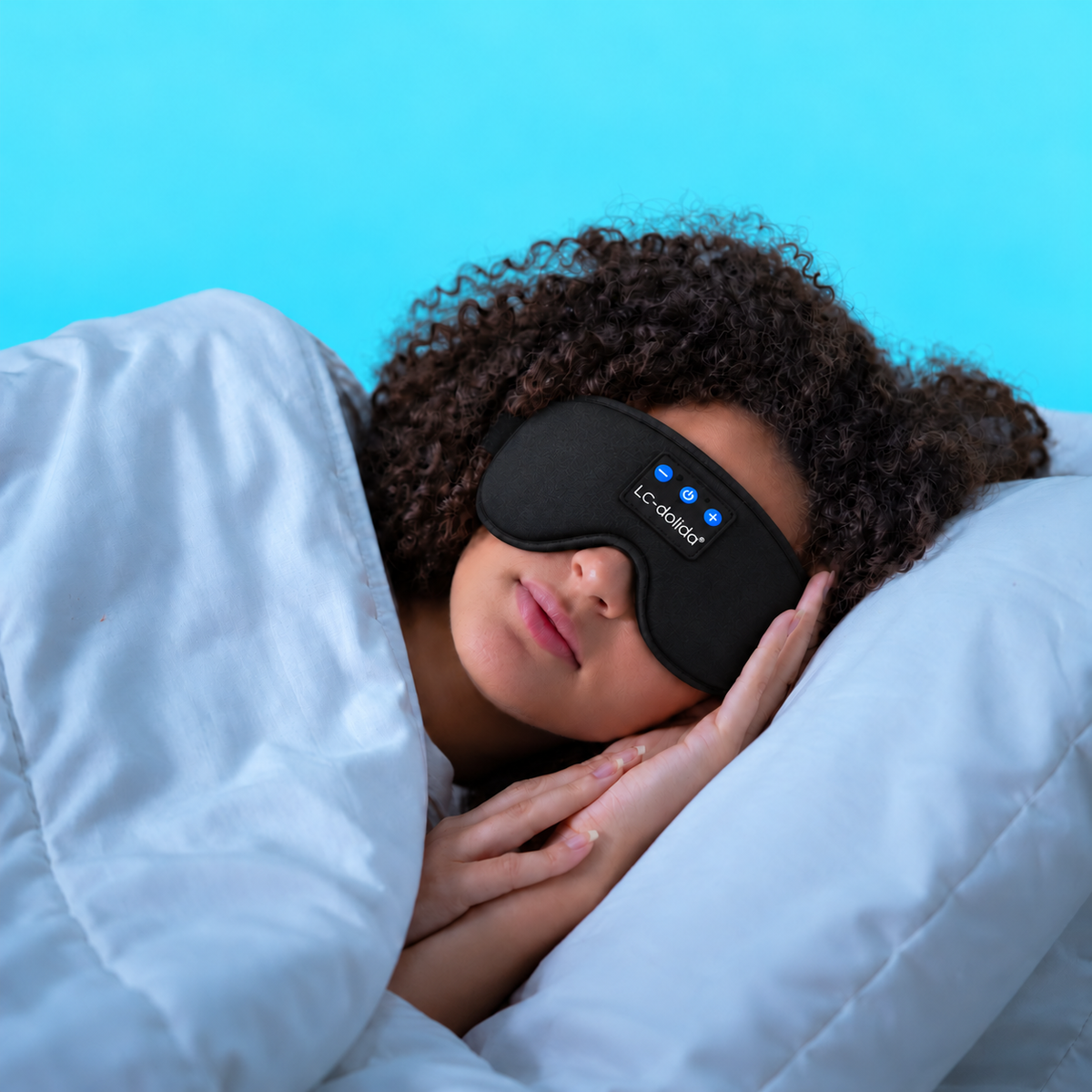 Woman lying on her side in bed wearing a black Bluetooth sleep mask